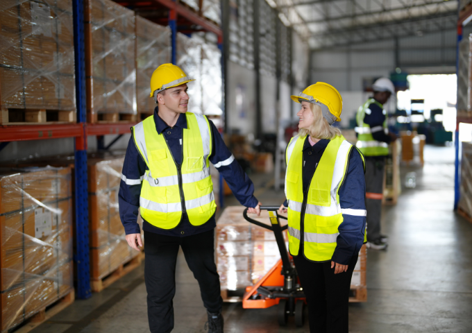 Two workers in high vis and hard-hats pulling a tray of products.