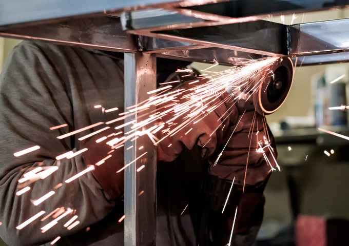 Pair of gloved hands grinding down a steal bench in a factory.