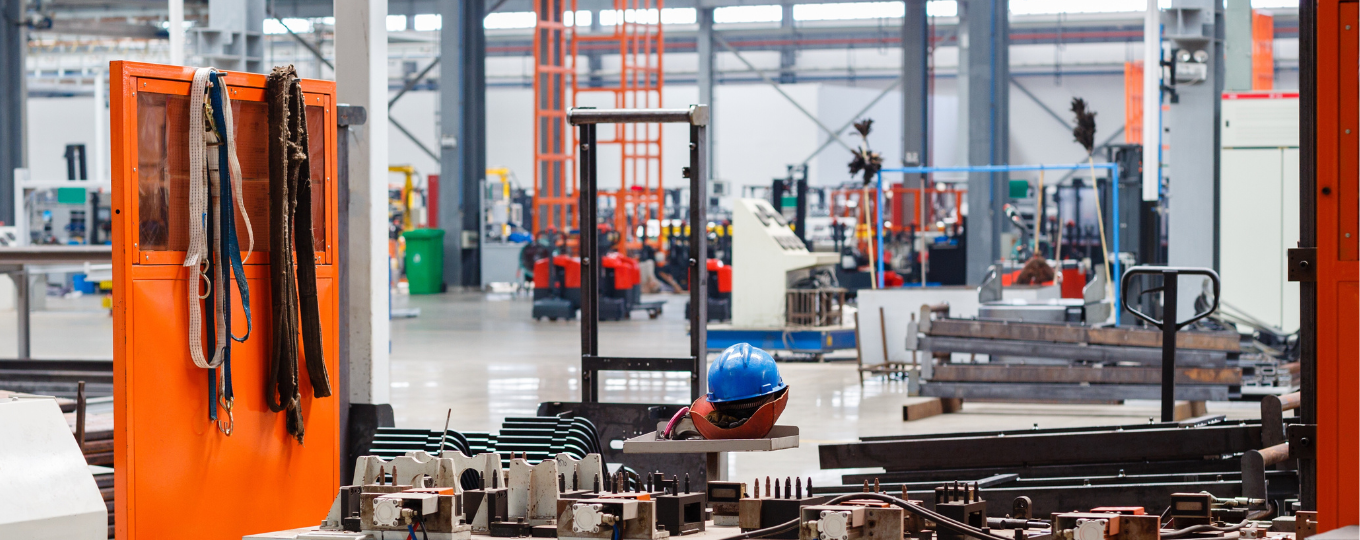 Photo of factory, machine equipment and a hard hat in the foreground. A bright orange door stands to the left, clearly in production.