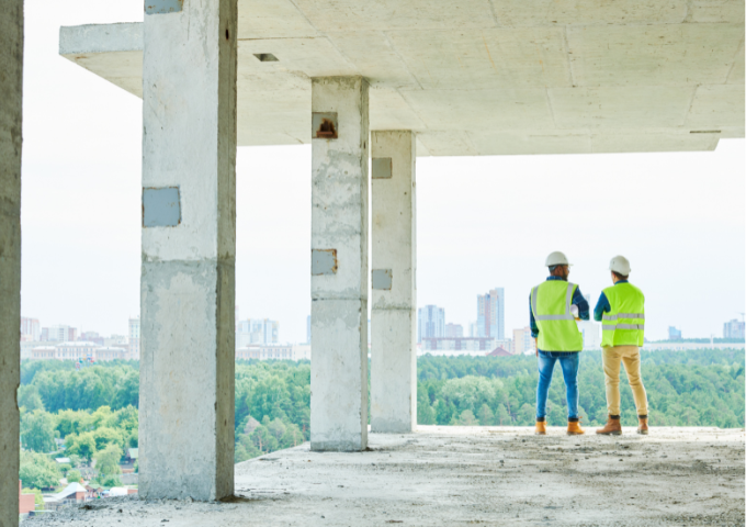 Two men in high vis on the concrete floor of a building overlooking the rainforest, backs to camera