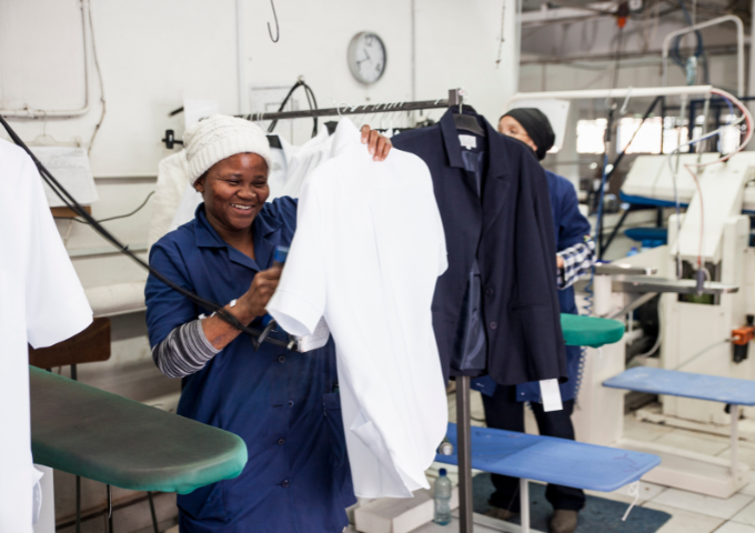 A photo of a garment factory worker smiling whilst holding up a shirt.