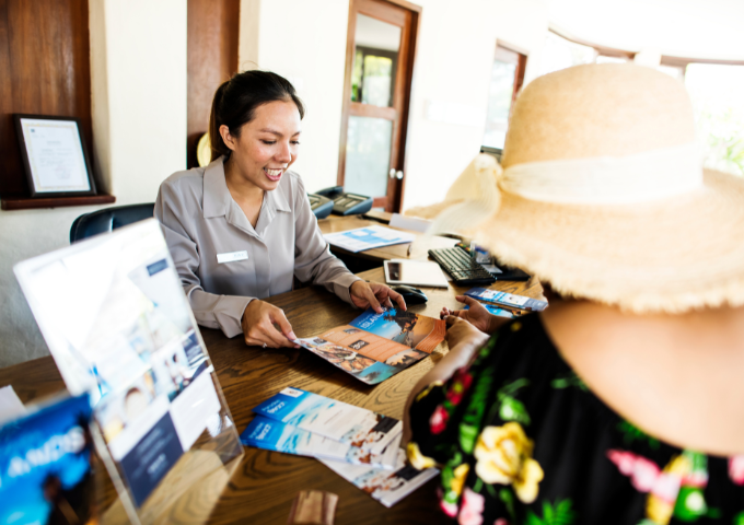 A receptionist at a hotel shows a tourist a brochure.